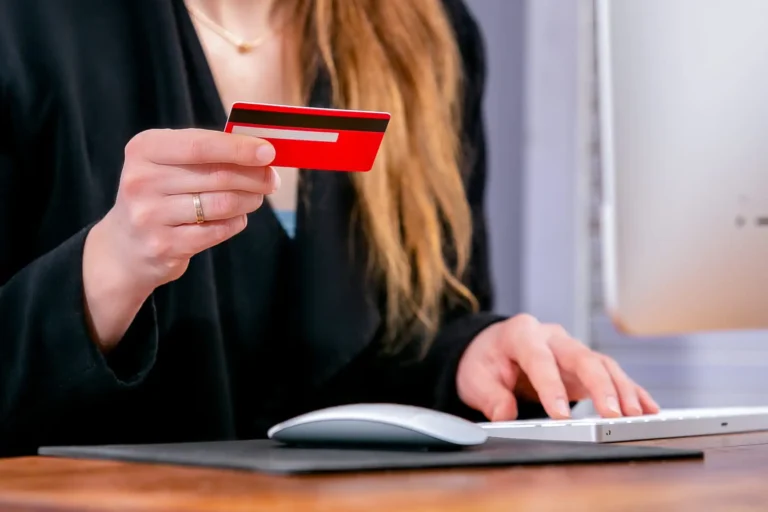 A person holding a red credit card while using a computer.