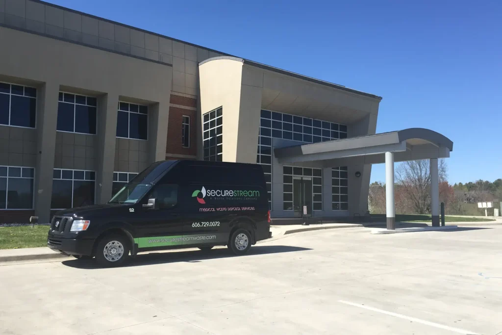 A black SecureStream medical waste disposal van parked in front of a modern office building.