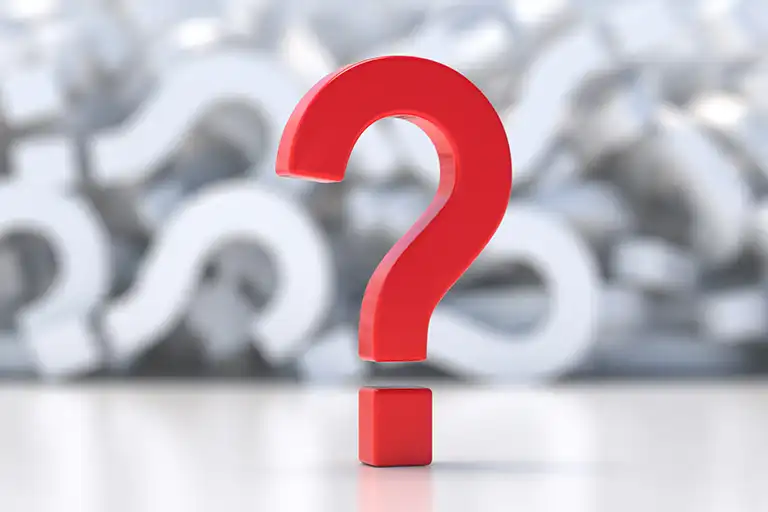 A large, red, three-dimensional question mark stands in focus before a blurred pile of white question marks.