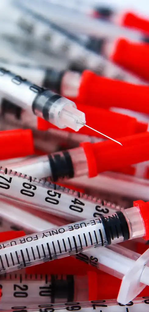 A pile of medical syringes with orange caps.