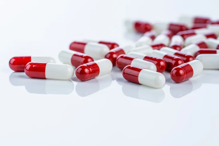 A scattered pile of red and white medicinal capsules on a white surface.