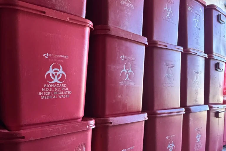 Multiple red plastic medical waste containers stacked in rows, each marked with a biohazard symbol and BIOHAZARD text.
