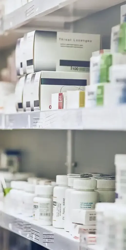 Shelves in a pharmacy stocked with various medicine boxes and white pill bottles.