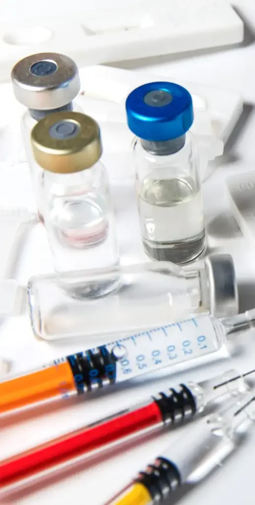 Medical glass vials with colorful caps, syringes filled with colored liquids, and rapid test kits.